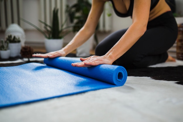 Crop woman rolling up yoga mat