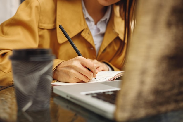 Crop woman taking notes in notepad while working in street cafe