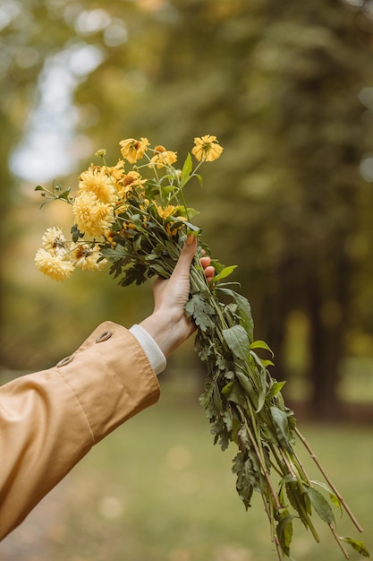 Crop woman with bouquet of yellow flowers in hand in autumn park