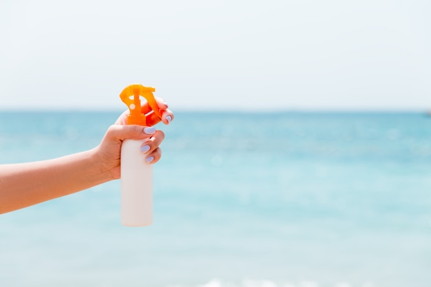 Croped image of woman's hand holding sunblock spray at the beach.