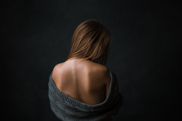 Photo croped portrait of a young blonde slim girl with naked waist. posing in the dark.