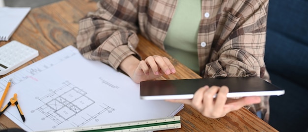 Photo cropped architect woman working with digital tablet and blueprint in office room.