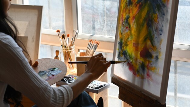 Cropped back image of young beautiful artist holding a brush and drawing on painting canvas