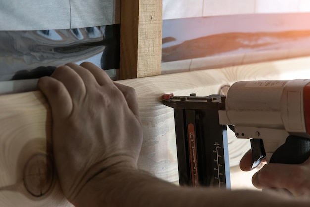 Обрезанные руки строителя держат пневматический гвоздезабивной степлер для деревянной доски.