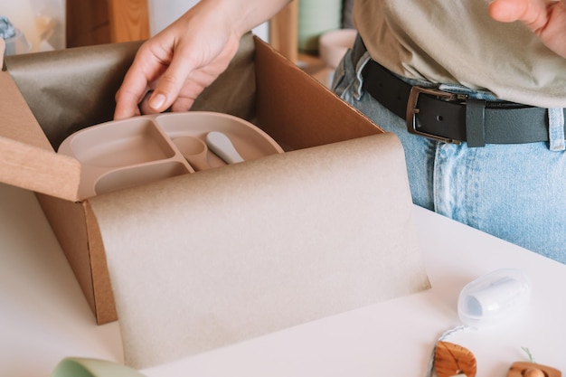 Cropped businesswoman hands packing and wrapping shipment with silicone kids dishes in cardboard box Workshop store