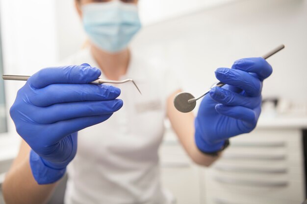 Cropped close up of female dentist holding out dental instruments to the camera