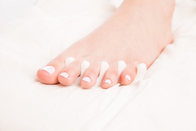 Foto ritagliato da vicino il piede femminile sulla procedura di pedicure posa su lenzuolo bianco.