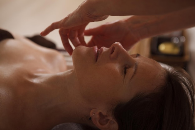 Cropped close up of a mature woman relaxing during professional face massage treatment at spa center