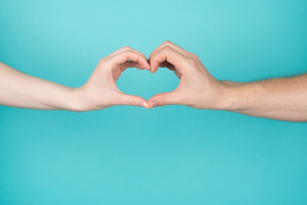 Cropped close-up photo of woman and man making heart with their hands isolated on blue teal bright color background