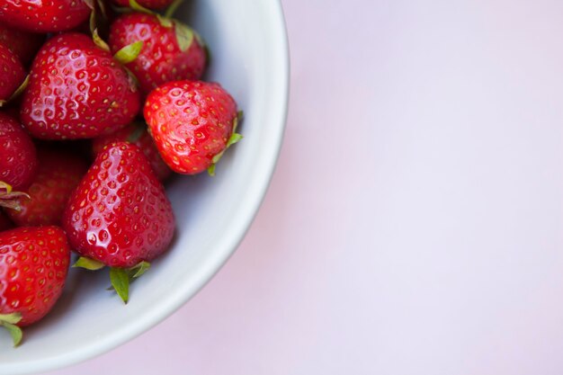 Cropped close up of strawberries in a bowl on light pink background, copy space