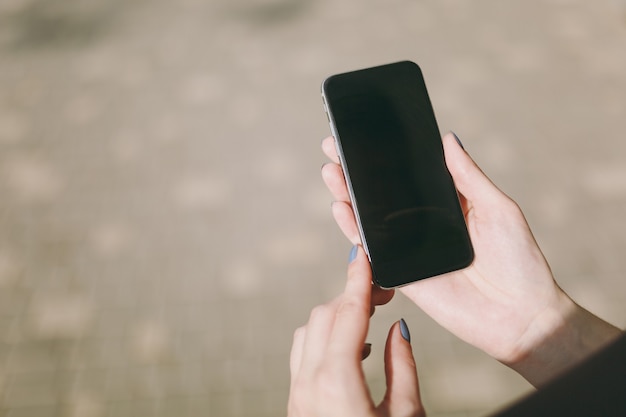 Ritagliato primo piano delle mani della donna che tengono e utilizzano il telefono cellulare, smartphone con schermo vuoto vuoto nel parco cittadino all'aperto