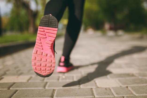 Cropped close up of woman legs in sportswear, black and pink sneakers doing sport exercises, training and jogging on path outdoors