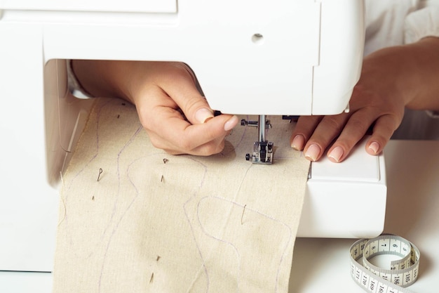 Cropped closeup hands of tailor woman using sewing machine inserting textile pattern with stitch contours under needle