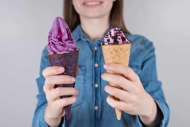 Cropped closeup photo of delightful satisfied dreamy lovely girl holding two colorful ice creams in hands isolated grey background