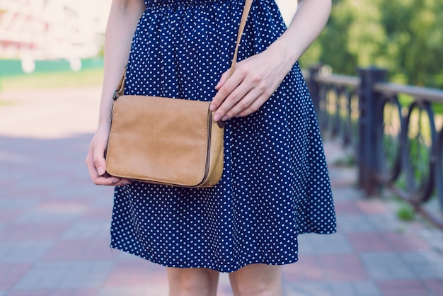 Cropped closeup photo of slim attractive charming gorgeous happy nice slender girl touching small little luxurious shoulder bag standing outside having good mood