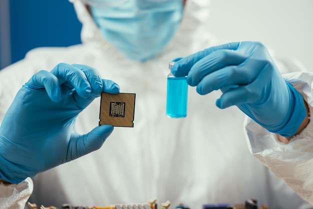 푸른 액체로 컴퓨터 마이크로칩과 유리 용기를 들고 있는 엔지니어의 자른 모습