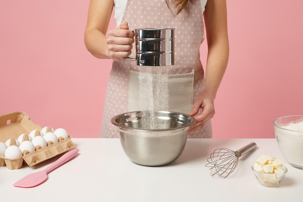 Photo cropped female chef cook confectioner or baker in apron white t-shirt, toque chefs hat cooking cake or cupcake at table isolated on pink pastel background in studio. mock up copy space food concept.