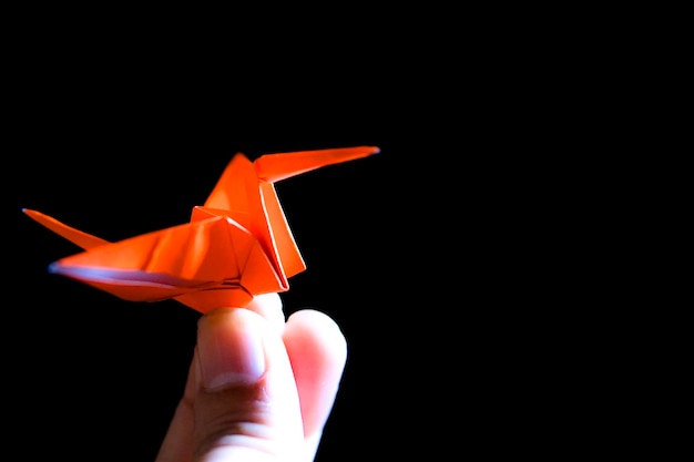 Cropped finger of person holding paper crane against black background