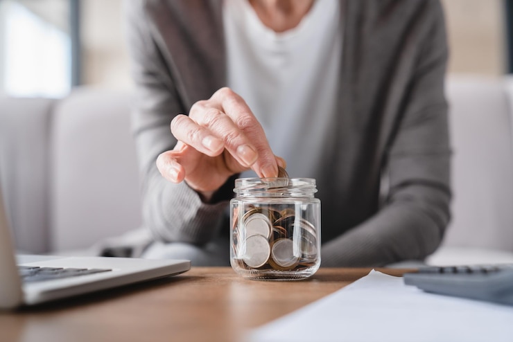 Photo cropped focused shot savings concept nest egg of old elderly senior woman grandmother saving money economizing pension mortgage loan at home using laptop and putting coin into moneybox