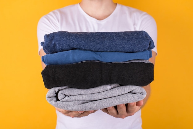 Cropped front view photo of man holding folded clothes giving you isolated on yellow background