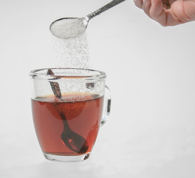 Фото Рука, добавляющая сахар в чай на белом фоне