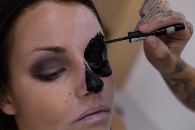 Cropped hand of beautician applying face paint to young woman