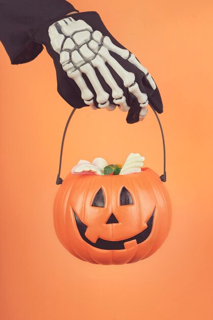 Cropped hand of boy with skeleton glove holding jack o lantern basket against orange background
