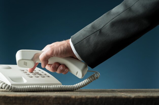 Photo cropped hand of businessman using landline phone on table