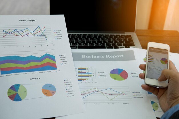 Cropped hand of businessman using phone at graph in office