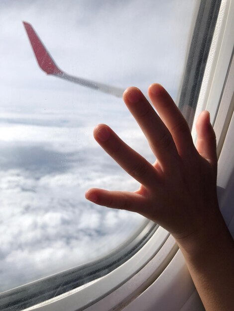 Foto mano tagliata di un bambino che tocca la finestra dell'aereo