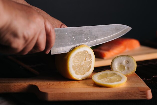 Photo cropped hand cutting lemon on board against black background