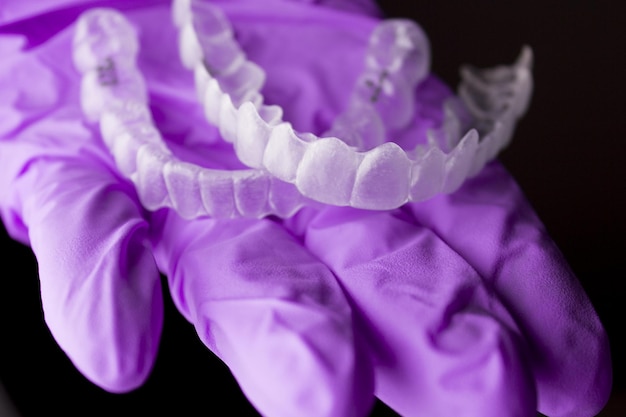 Cropped hand of dentist holding dental aligner against black background