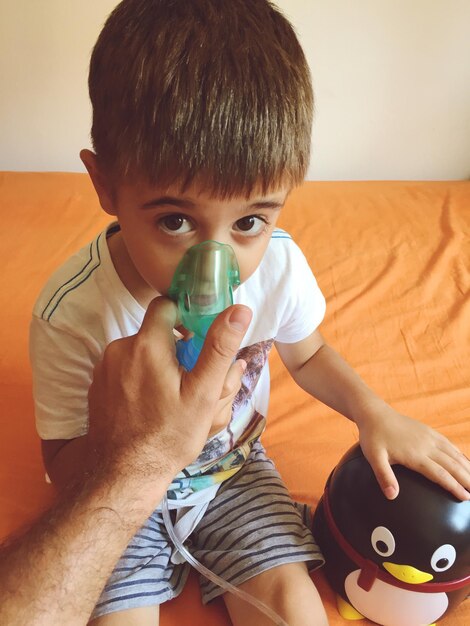 Photo cropped hand of father holding oxygen mask for son on bed