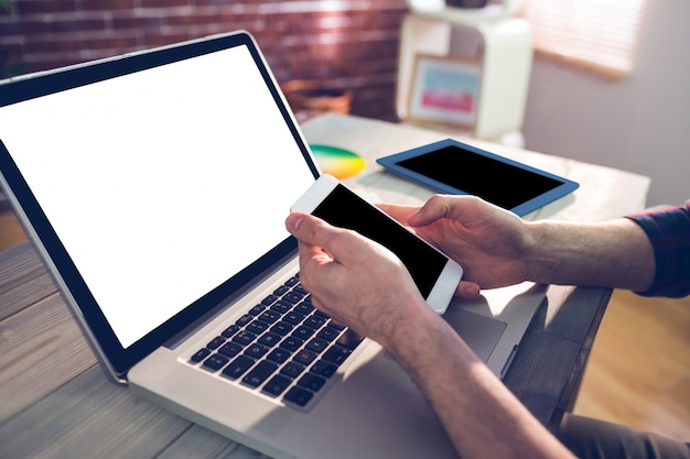 Cropped hand of graphic designer using smartphone and laptop