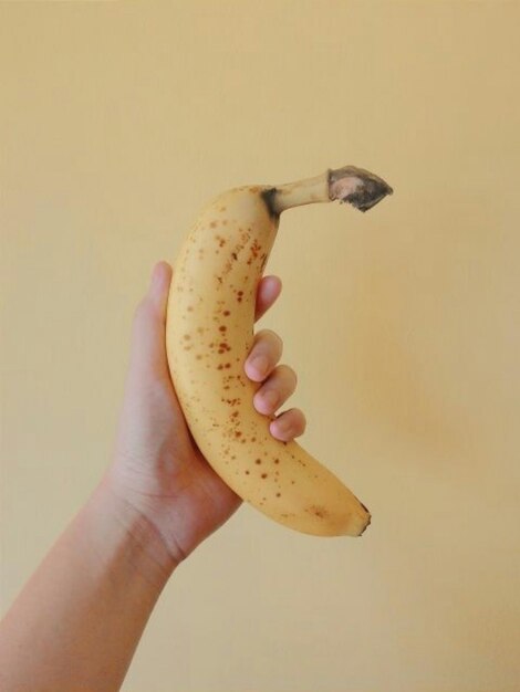 Foto mano tagliata che tiene una banana su uno sfondo beige