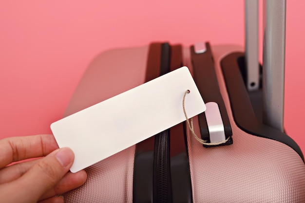 Cropped hand holding blank label on suitcase against pink background