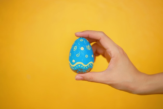 Cropped hand holding blue easter egg against wall