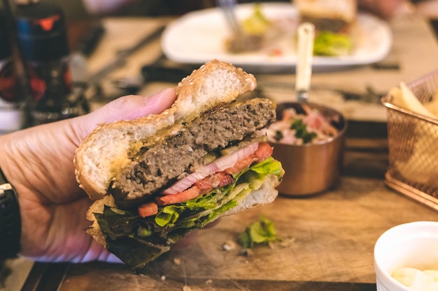 cropped hand holding burger over table