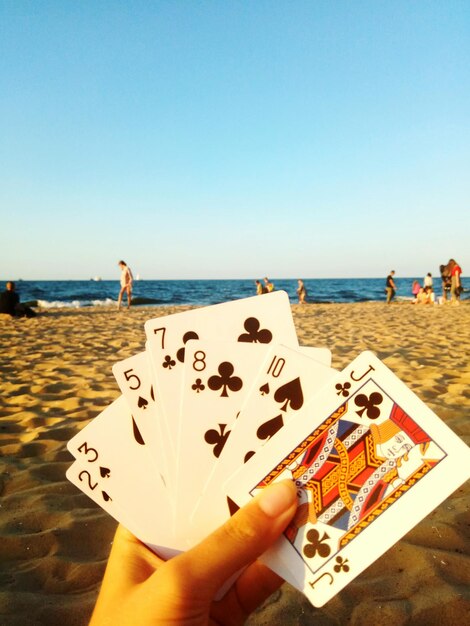 Foto mano tagliata che tiene una carta in spiaggia contro un cielo limpido