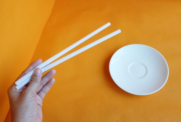 Cropped hand holding chopstick by empty plate on yellow background