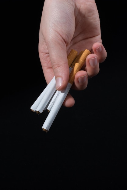 Cropped hand holding cigarettes against black background