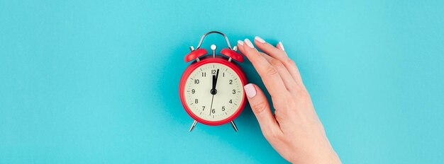 Cropped hand holding clock against blue background