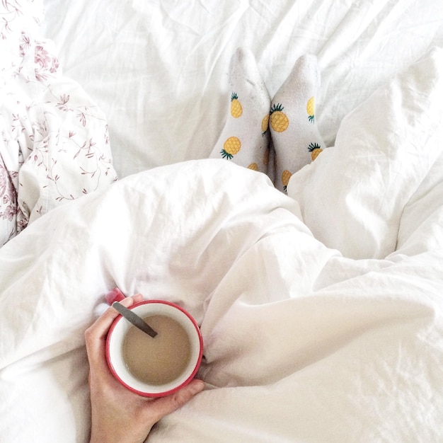 cropped hand holding coffee cup on bed at home