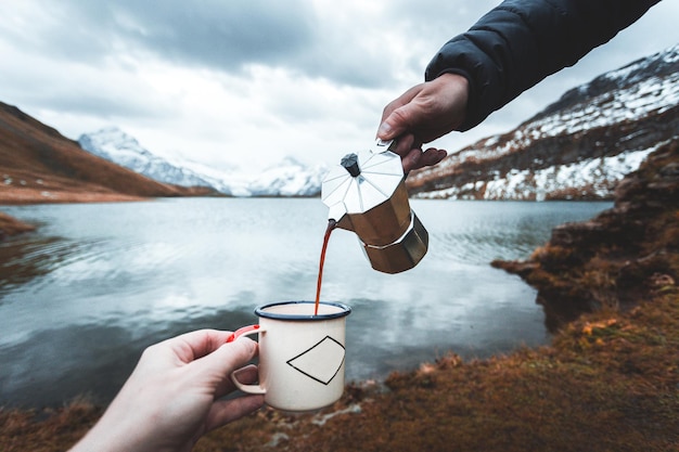 Photo cropped hand holding coffee cup while person pouring drink against sea