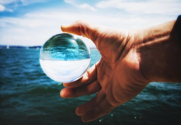 Foto mano tagliata che tiene una palla di cristallo contro il mare