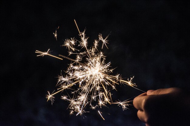 Foto mano tagliata che tiene in mano un fuoco d'artificio di notte