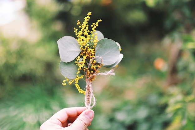 Cropped hand holding flowers and leaves tied up string