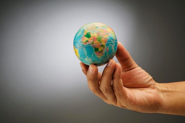 Cropped hand holding globe against gray background