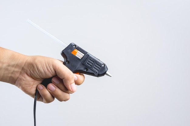 Cropped hand holding glue gun against gray background