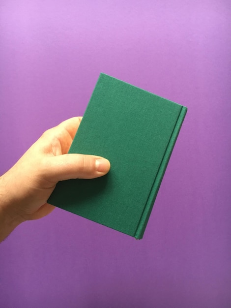 Cropped hand holding green book against purple background